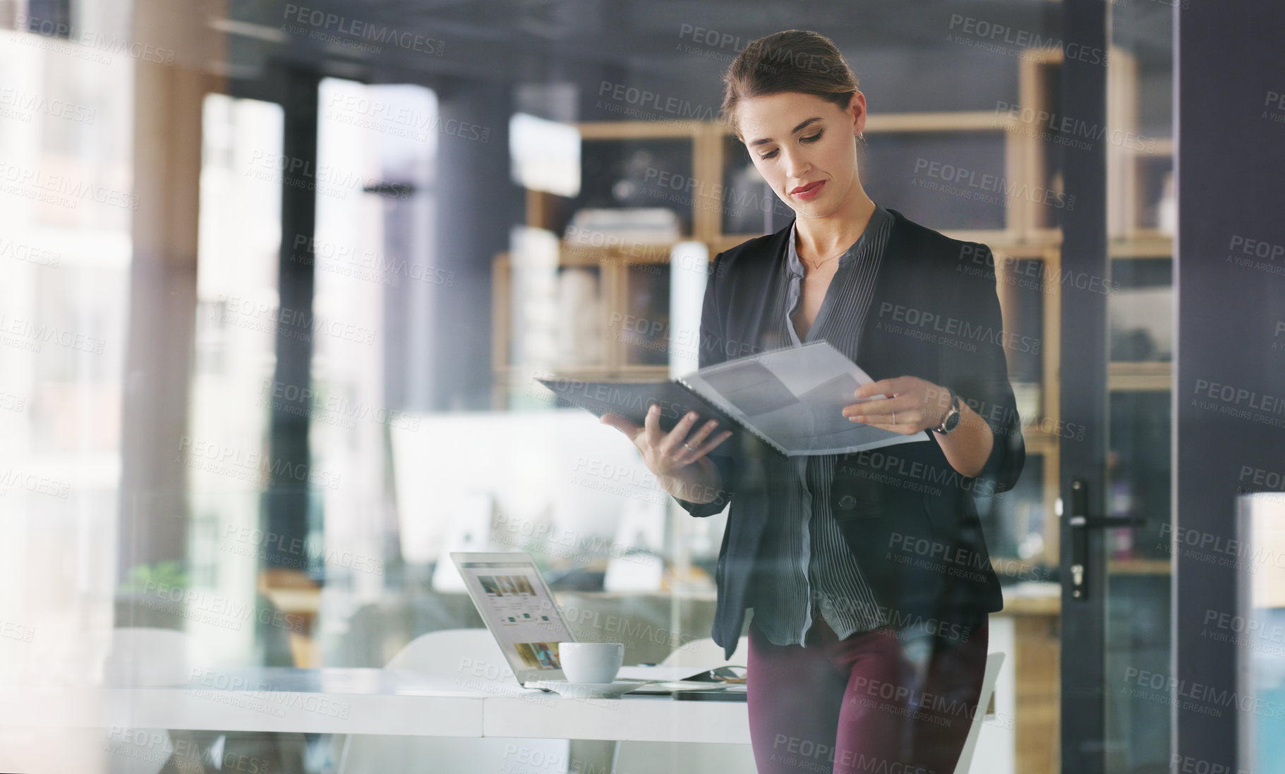 Buy stock photo Cropped shot of an attractive young businesswoman standing alone in her office and reading documents