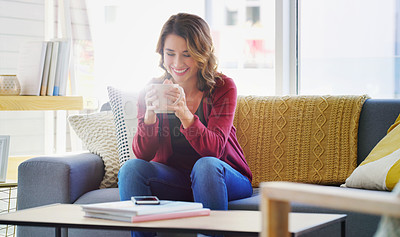 Buy stock photo Cropped shot of an attractive young woman sitting on her living room couch and holding a cup of coffee