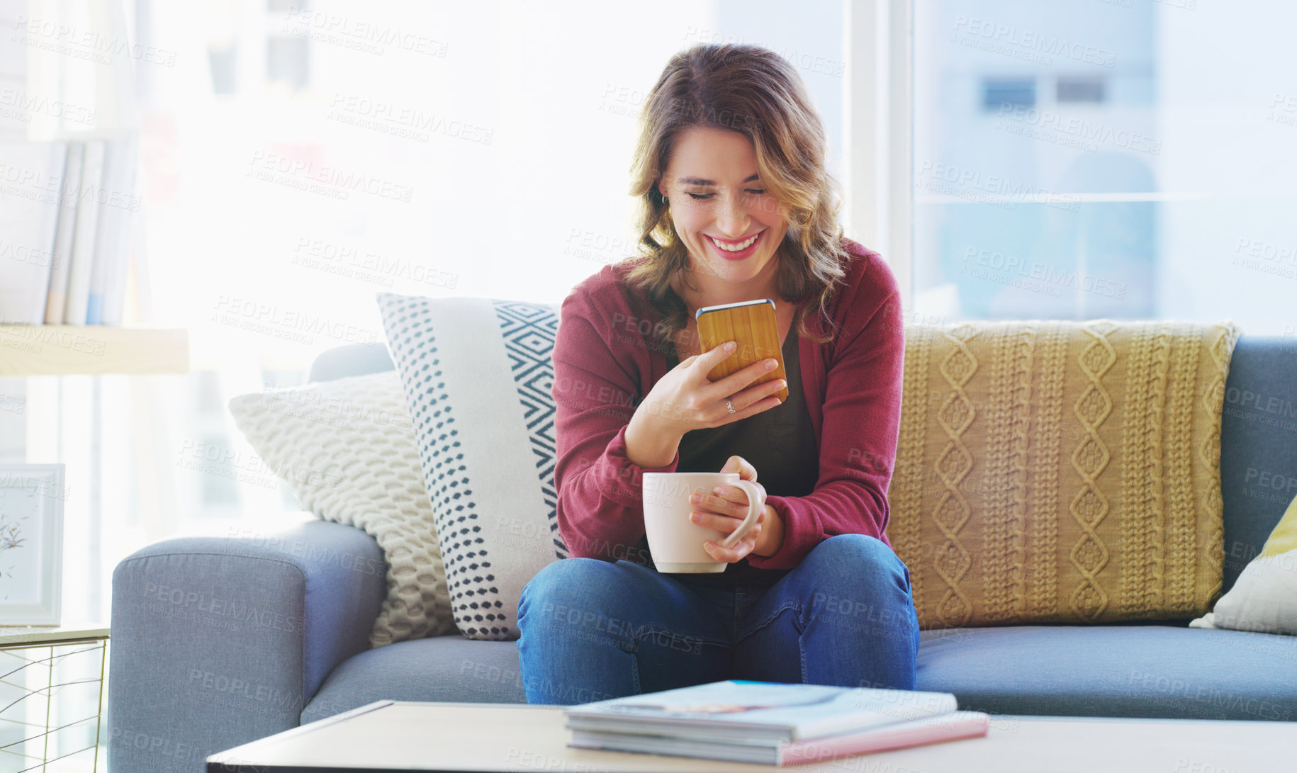 Buy stock photo Cropped shot of an attractive young woman sitting and using her cellphone while enjoying a cup of coffee at home