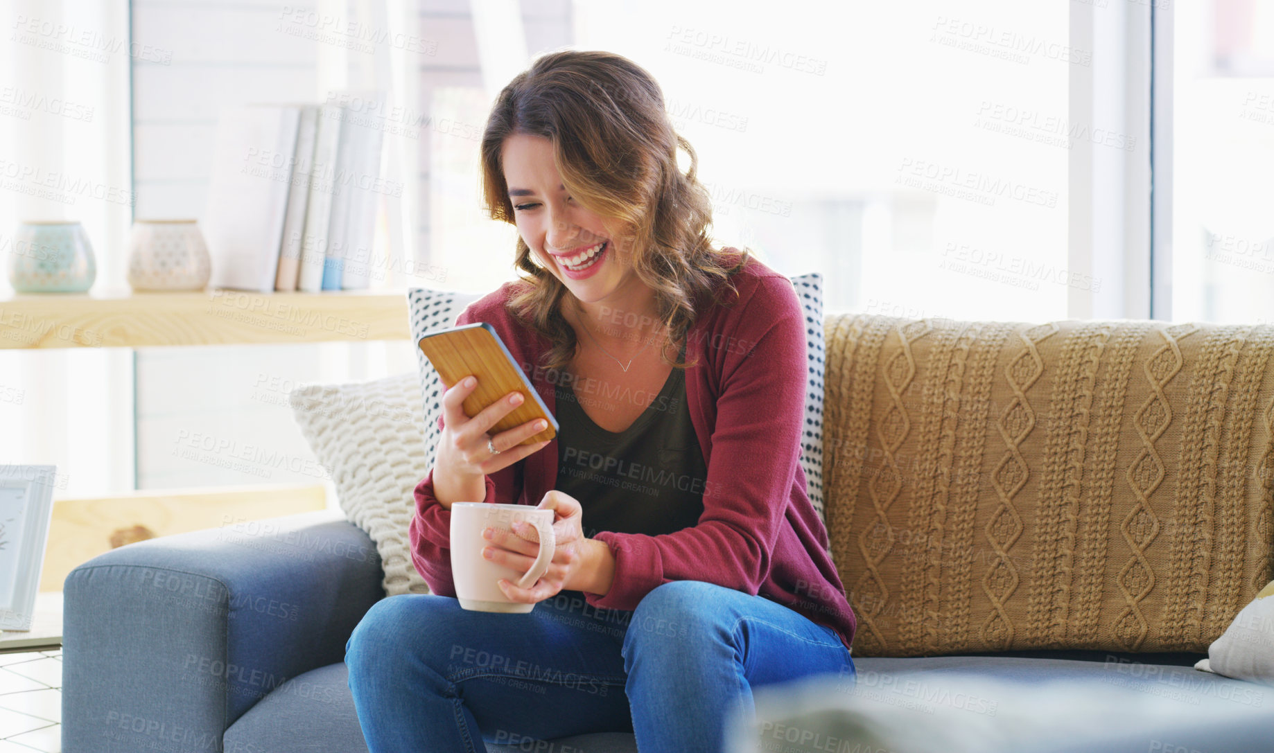Buy stock photo Cropped shot of an attractive young woman sitting and using her cellphone while enjoying a cup of coffee at home