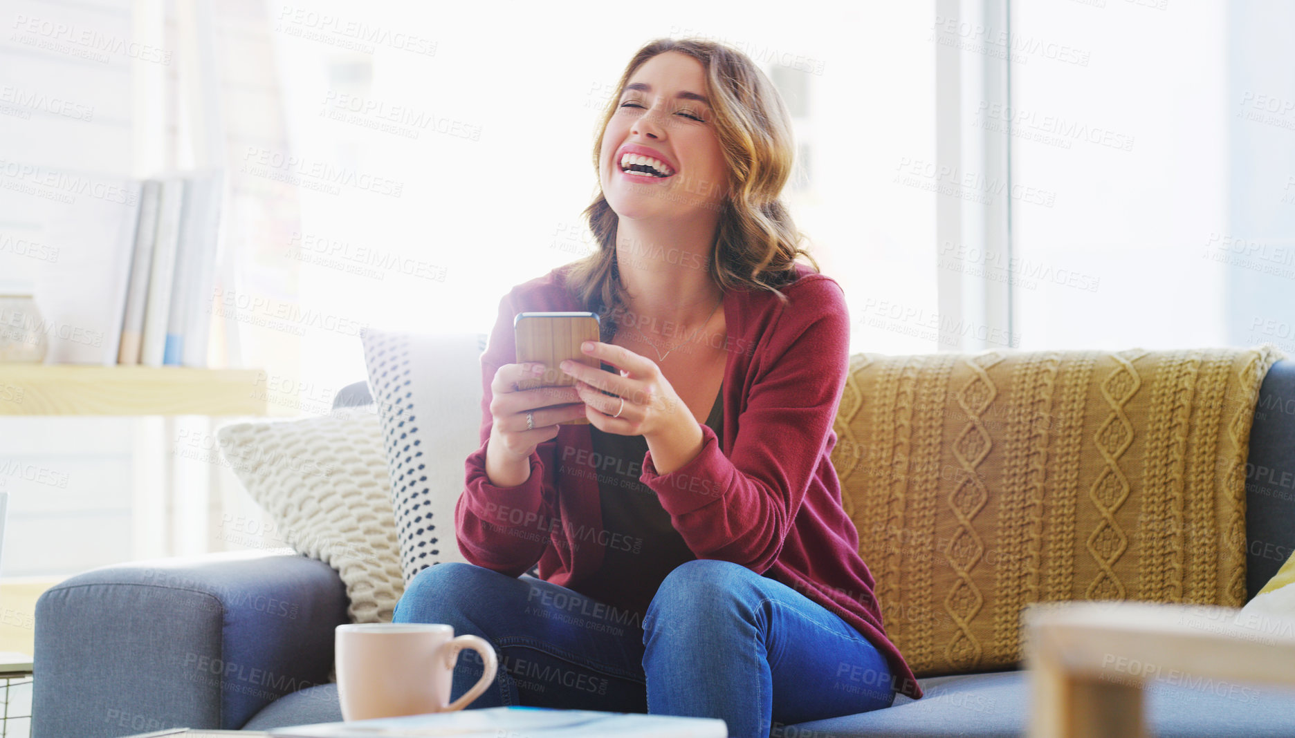 Buy stock photo Cropped shot of an attractive young woman sitting alone on the sofa in her living room and using her cellphone