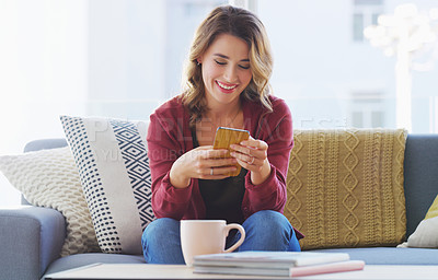 Buy stock photo Cropped shot of an attractive young woman sitting alone on the sofa in her living room and using her cellphone