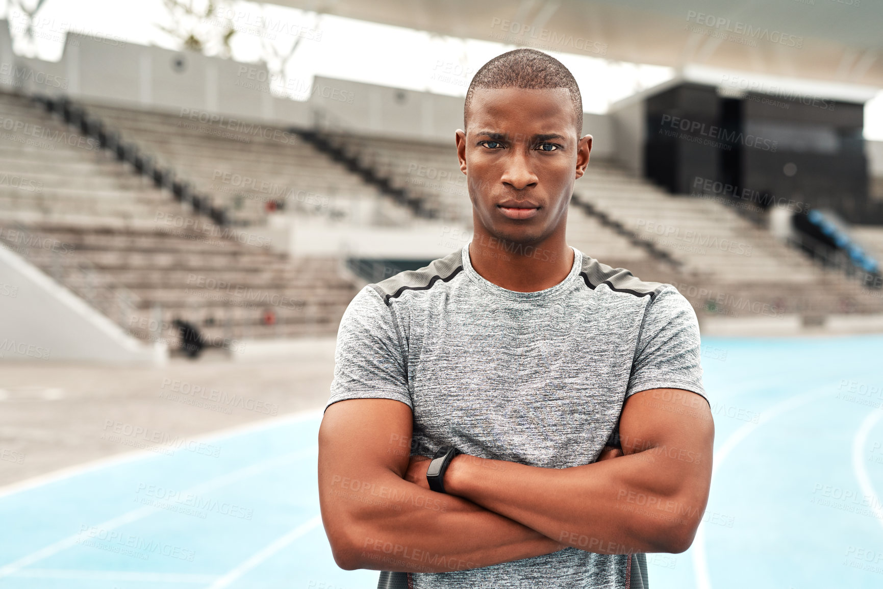 Buy stock photo Cropped portrait of a handsome young athlete standing alone with his arms folded before running a track field