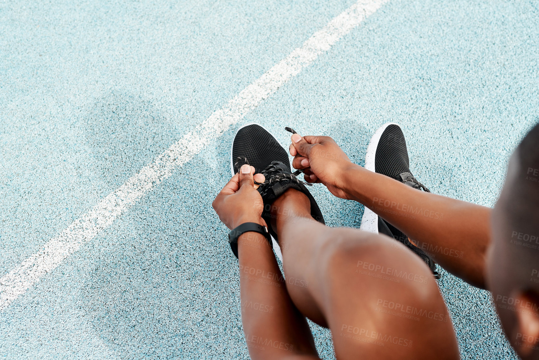 Buy stock photo Cropped shot of an unrecognizable athlete crouching down and tying his shoelaces before going for a run alone