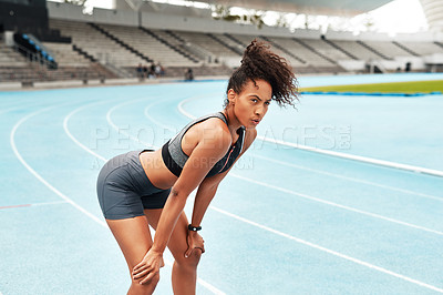 Buy stock photo Cropped shot of an attractive young athlete standing on a track field alone and catching her breath after running