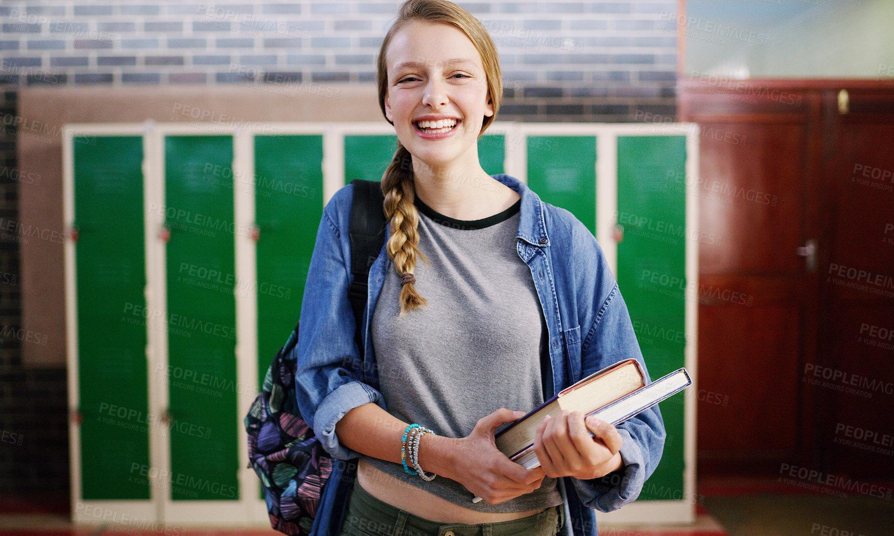 Buy stock photo Cropped shot of a cheerful young school kid holding her books while waiting to go to class inside of a school during the day