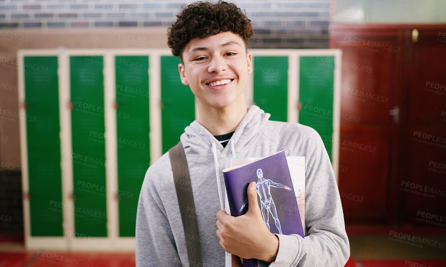 Buy stock photo Cropped shot of a cheerful young school kid holding his books while waiting to go to class inside of a school during the day