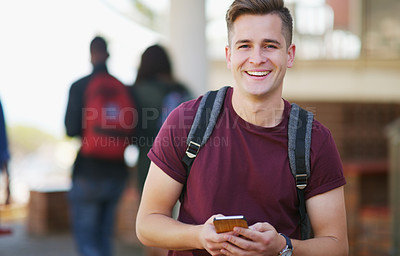Buy stock photo Portrait of a cheerful young student texting on his cellphone while waiting to go to class outside of a school during the day