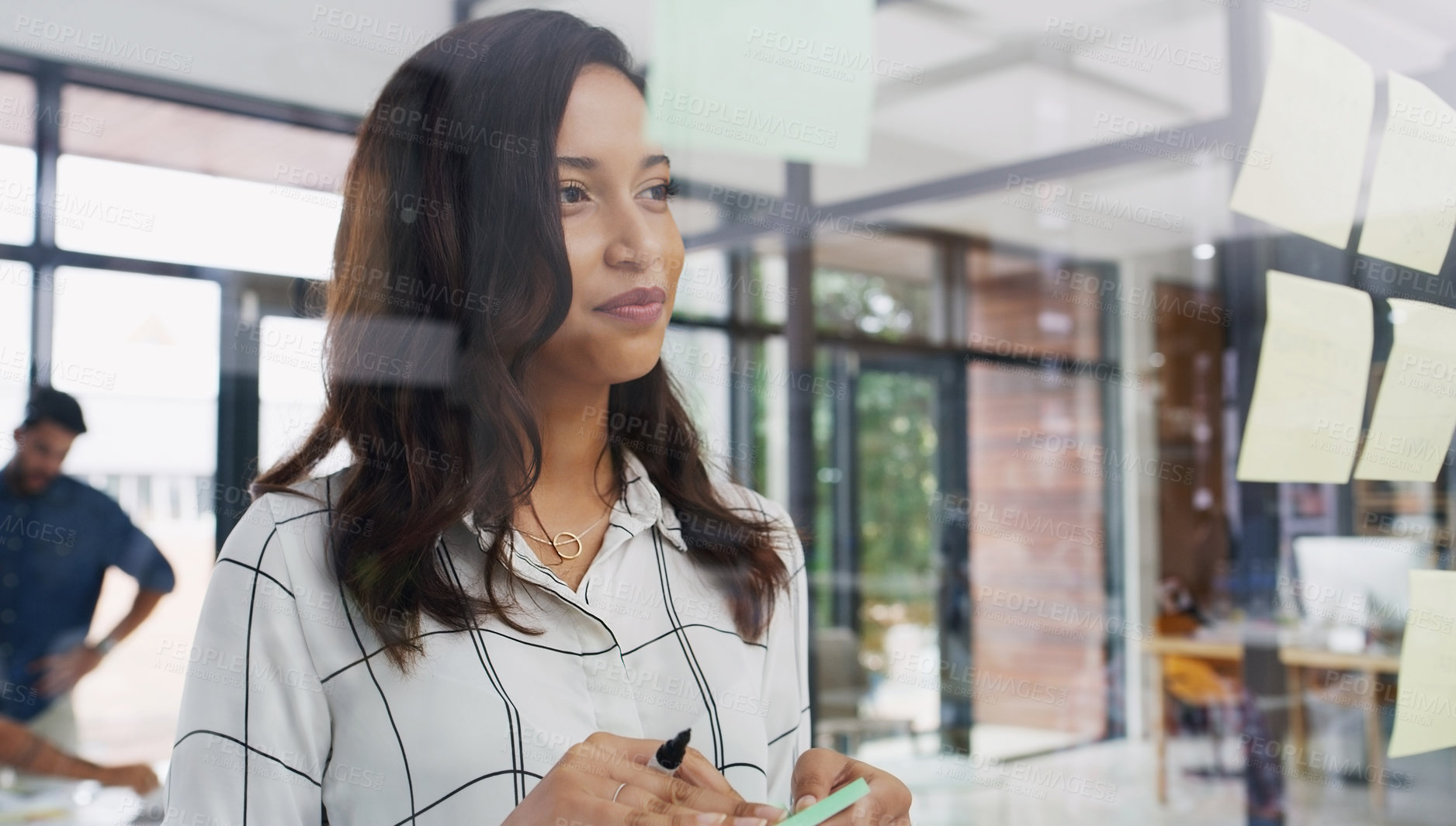 Buy stock photo Shot of a young businesswoman brainstorming with notes on a glass wall in an office