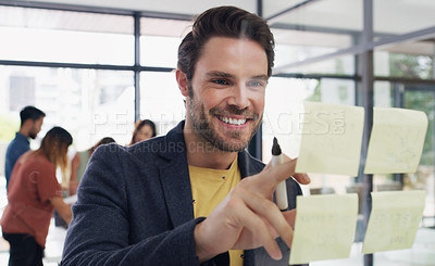 Buy stock photo Shot of a young businessman brainstorming with notes on a glass wall in an office