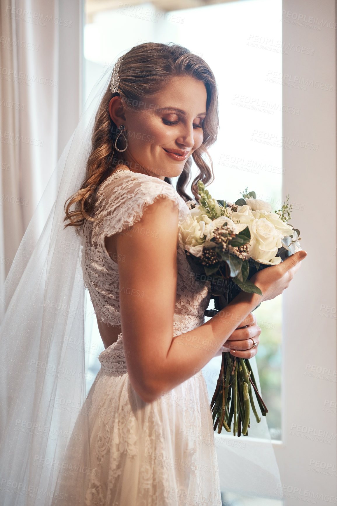 Buy stock photo Cropped shot of an attractive young bride standing alone in the dressing room and holding her bouquet of flowers