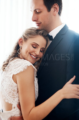 Buy stock photo Cropped shot of a happy young couple standing indoors and hugging each other affectionately after their wedding