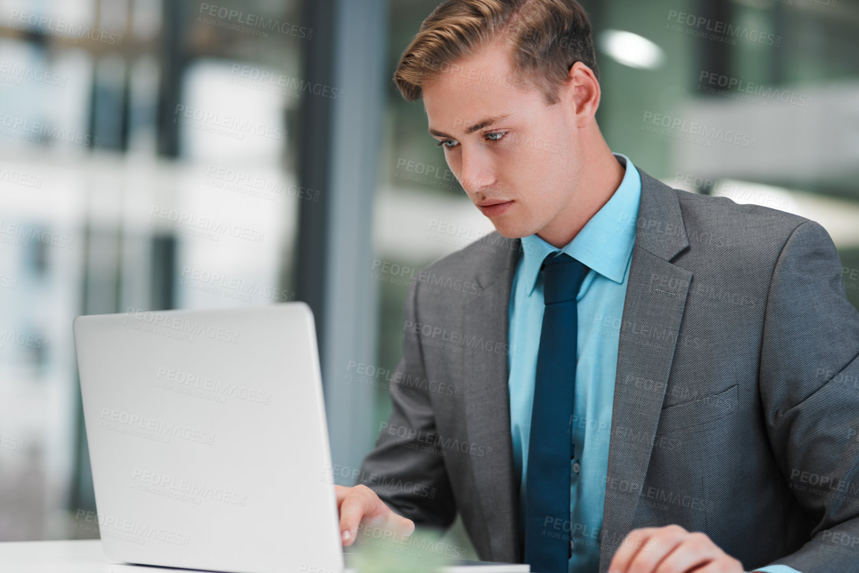 Buy stock photo Cropped shot of a handsome young businessman sitting alone in his office and using his laptop