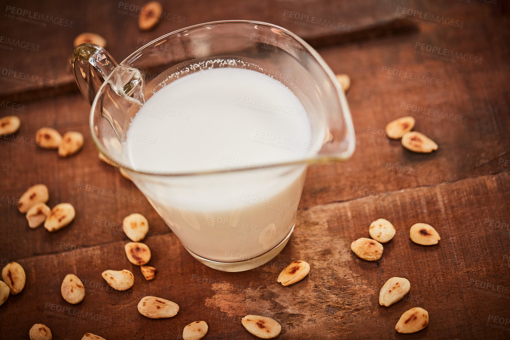 Buy stock photo Shot of a jug of milk surrounded by nuts on a table