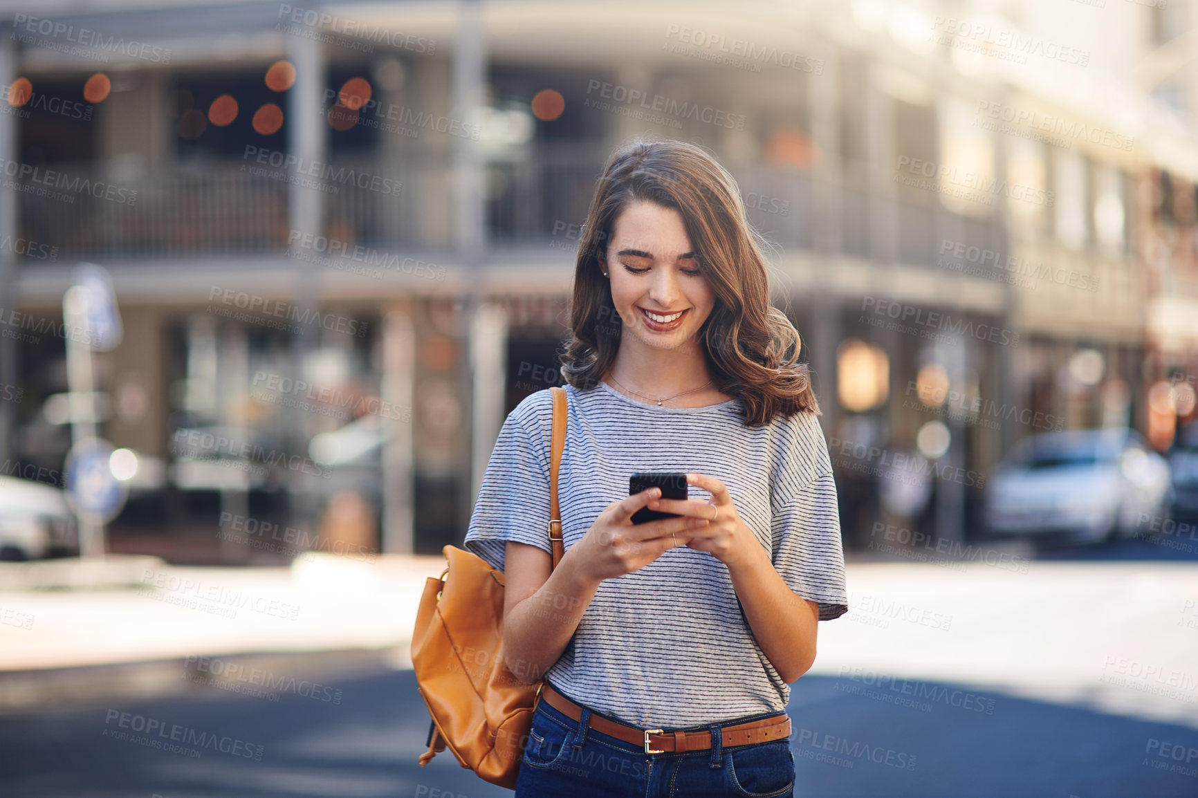 Buy stock photo Cropped shot of an attractive young woman sending text messages while spending her day out in the city