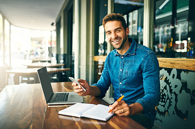 Buy stock photo Cropped portrait of a handsome young businessman sitting alone and making notes while using his cellphone in a cafe