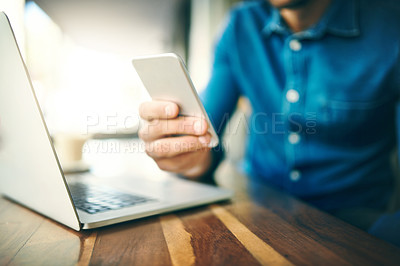 Buy stock photo Cropped shot of an unrecognizable businessman sitting and using his cellphone before working on his laptop in a cafe