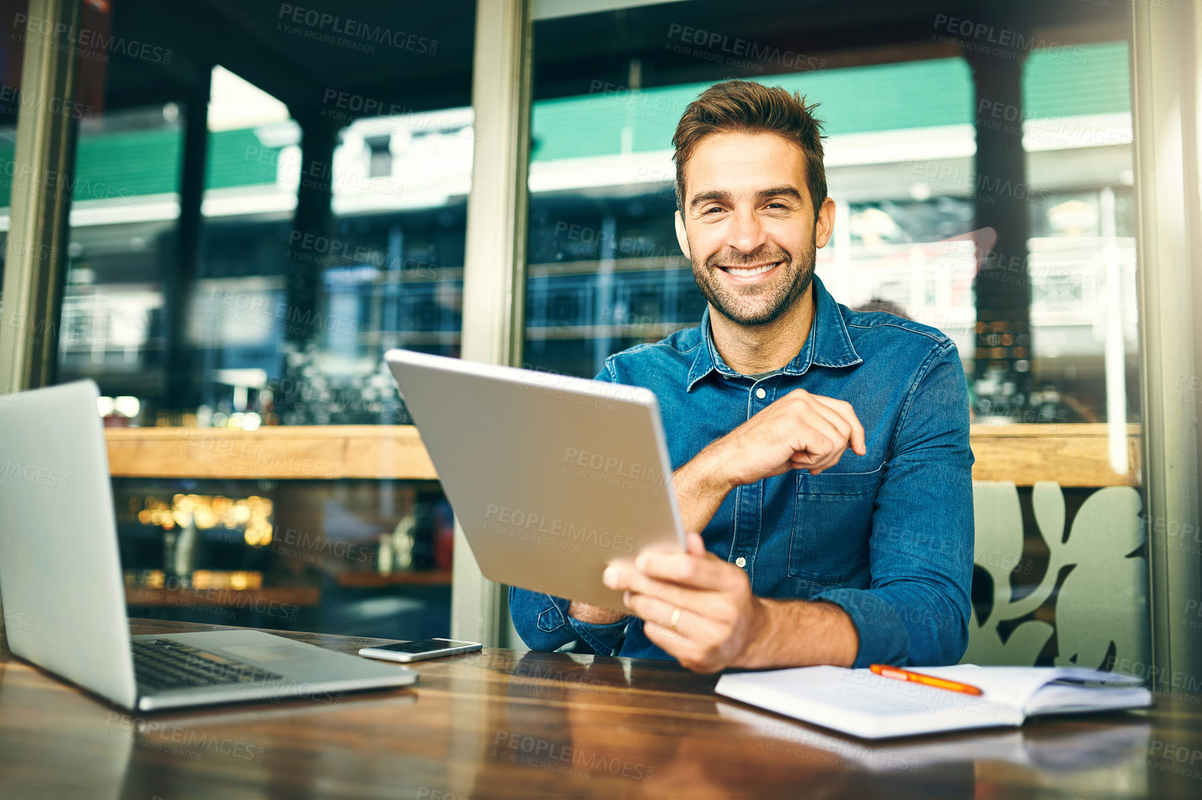 Buy stock photo Cropped portrait of a handsome young businessman sitting alone in a cafe and using a tablet