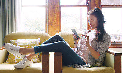 Buy stock photo Full length shot of an attractive young woman using a smartphone while relaxing on her couch at home