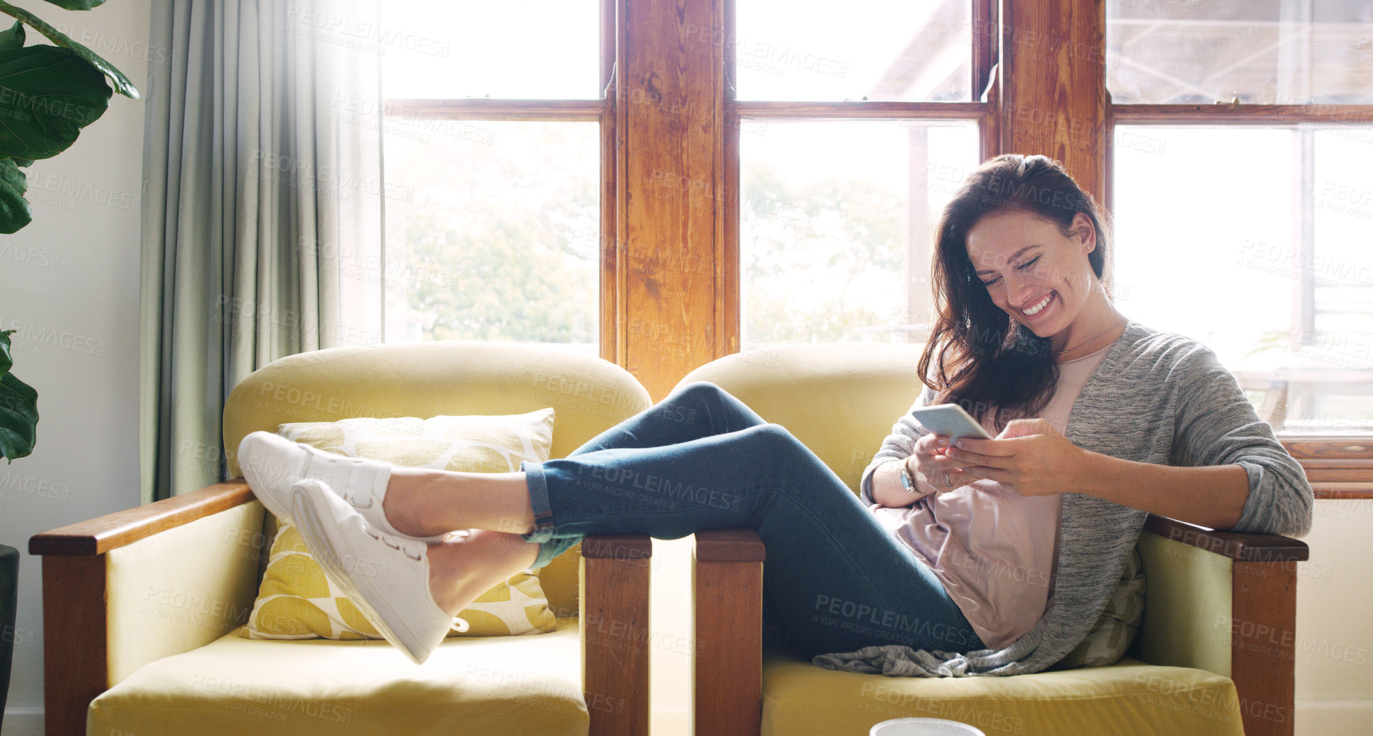 Buy stock photo Full length shot of an attractive young woman smiling while using a smartphone on her couch at home