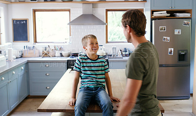 Buy stock photo Cropped shot of an affectionate young boy smiling at his father while sitting on the kitchen counter at home