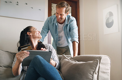 Buy stock photo Cropped shot of an affectionate young woman smiling at her husband while using a digital tablet to shop online at home