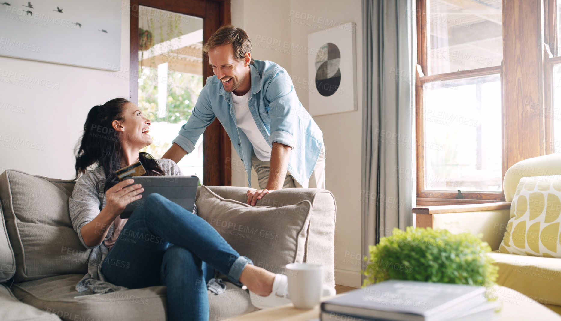Buy stock photo Cropped shot of an affectionate young woman laughing with her husband while using a digital tablet to shop online at home