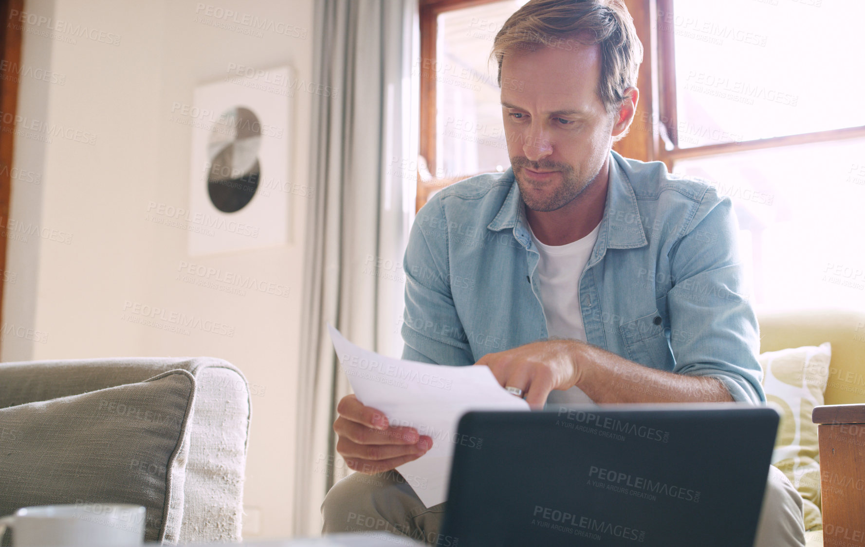 Buy stock photo Cropped shot of a handsome young man looking thoughtful while going through his budget at home