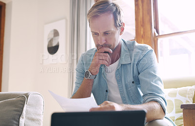 Buy stock photo Cropped shot of a handsome young man looking thoughtful while going through his budget at home