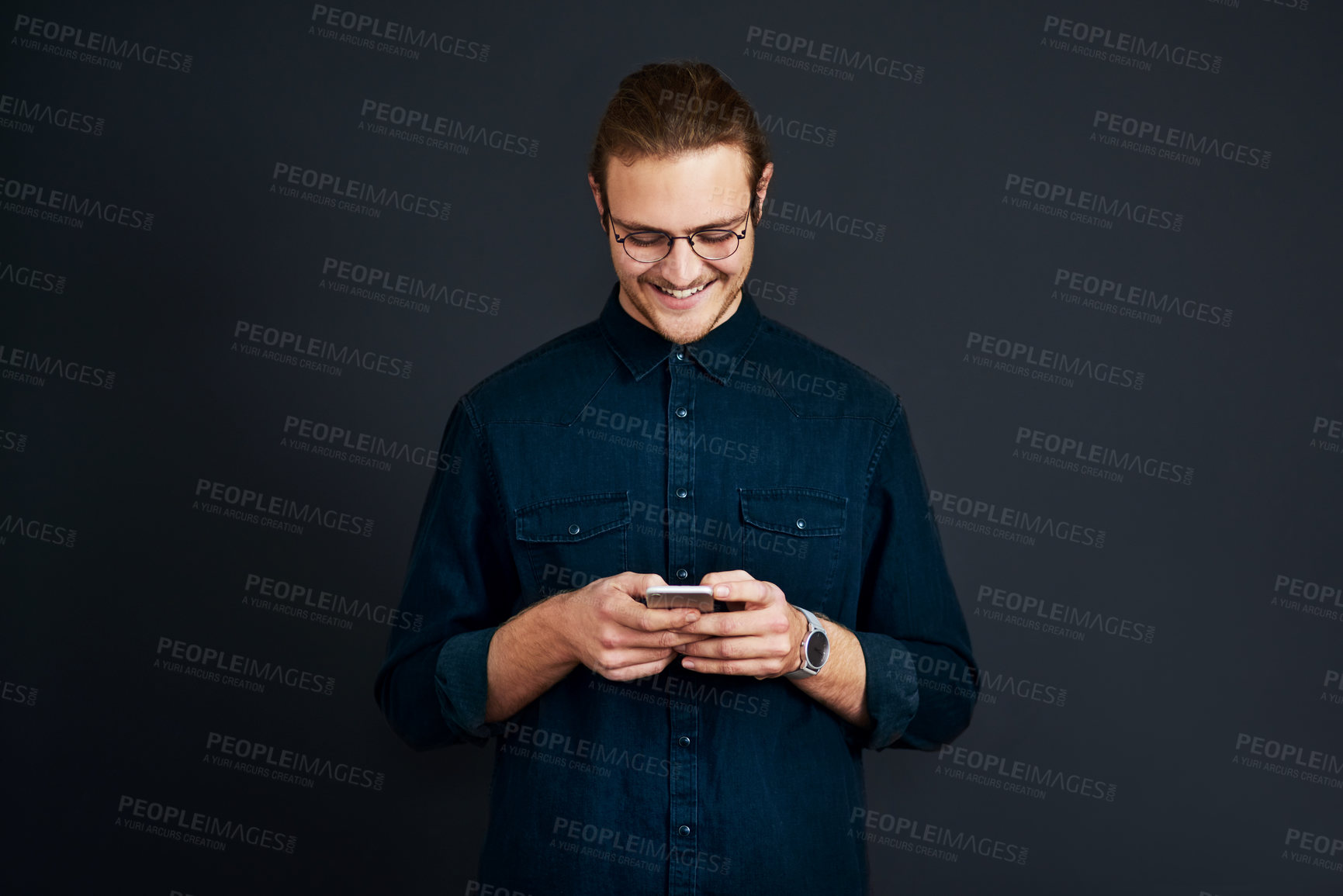 Buy stock photo Cropped shot of a handsome young businessman standing alone and texting on his cellphone against a black studio background