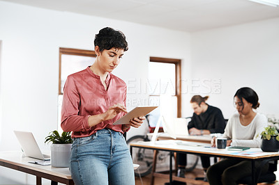 Buy stock photo Cropped shot of an attractive young businesswoman using a tablet while her colleagues work behind her in the office