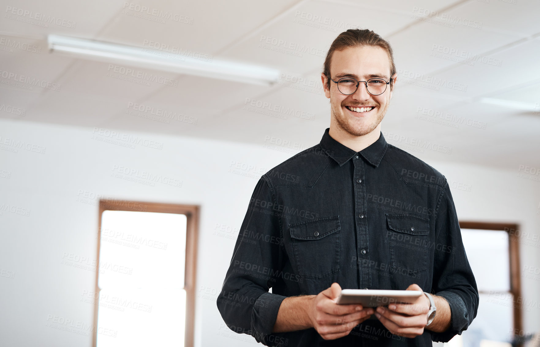 Buy stock photo Cropped portrait of a handsome young businessman standing and using a tablet in his office alone