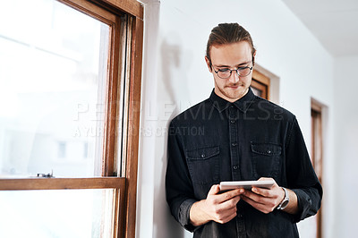 Buy stock photo Cropped shot of a handsome young businessman standing and using a tablet in his office alone