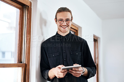Buy stock photo Cropped portrait of a handsome young businessman standing and using a tablet in his office alone