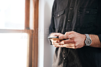 Buy stock photo Cropped shot of an unrecognizable businessman standing alone in his office and texting on his cellphone