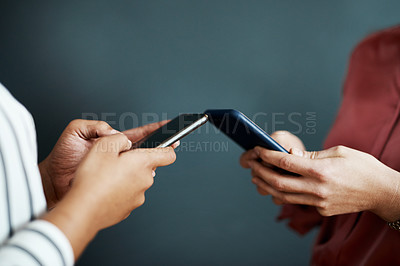 Buy stock photo Cropped shot of two unrecognizable businesswomen standing against a gray background and texting on their cellphones