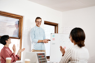 Buy stock photo Cropped shot of a handsome young businessman standing and writing on a white board while his colleagues clap for him