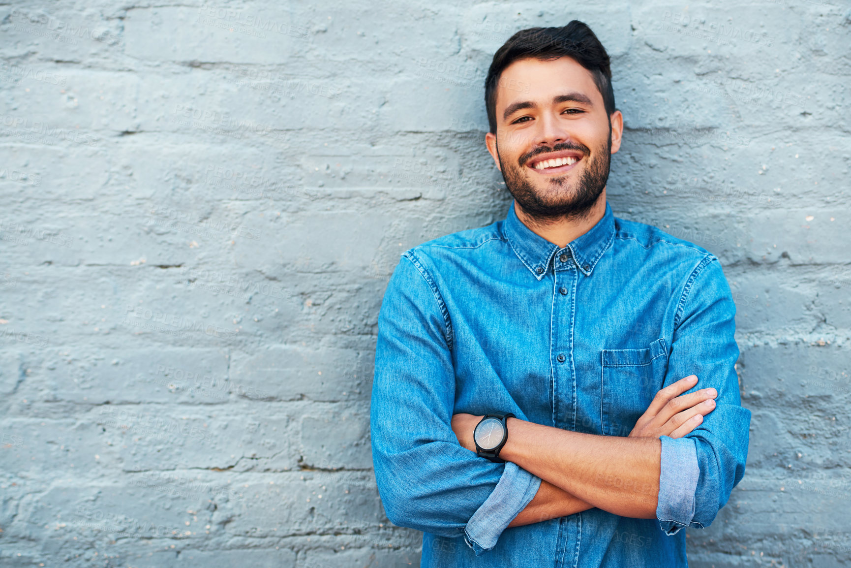 Buy stock photo Cropped portrait of a handsome young man smiling while standing with his arms crossed against a brick wall