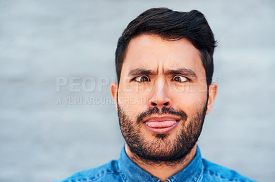 Buy stock photo Cropped shot of a handsome young man making funny faces while standing against a brick wall