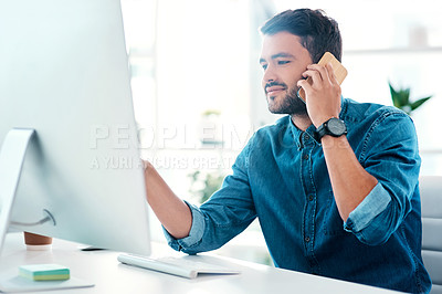 Buy stock photo Cropped shot of a handsome young businessman looking at a computer while taking a phonecall in an office