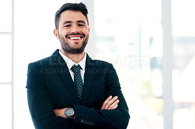 Buy stock photo Cropped portrait of a handsome young businessman smiling while standing with his arms crossed in a modern office