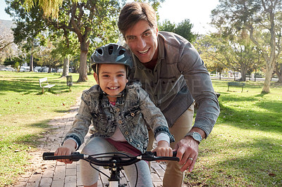 Buy stock photo Shot of an adorable little girl learning to ride a bicycle with her father in the park