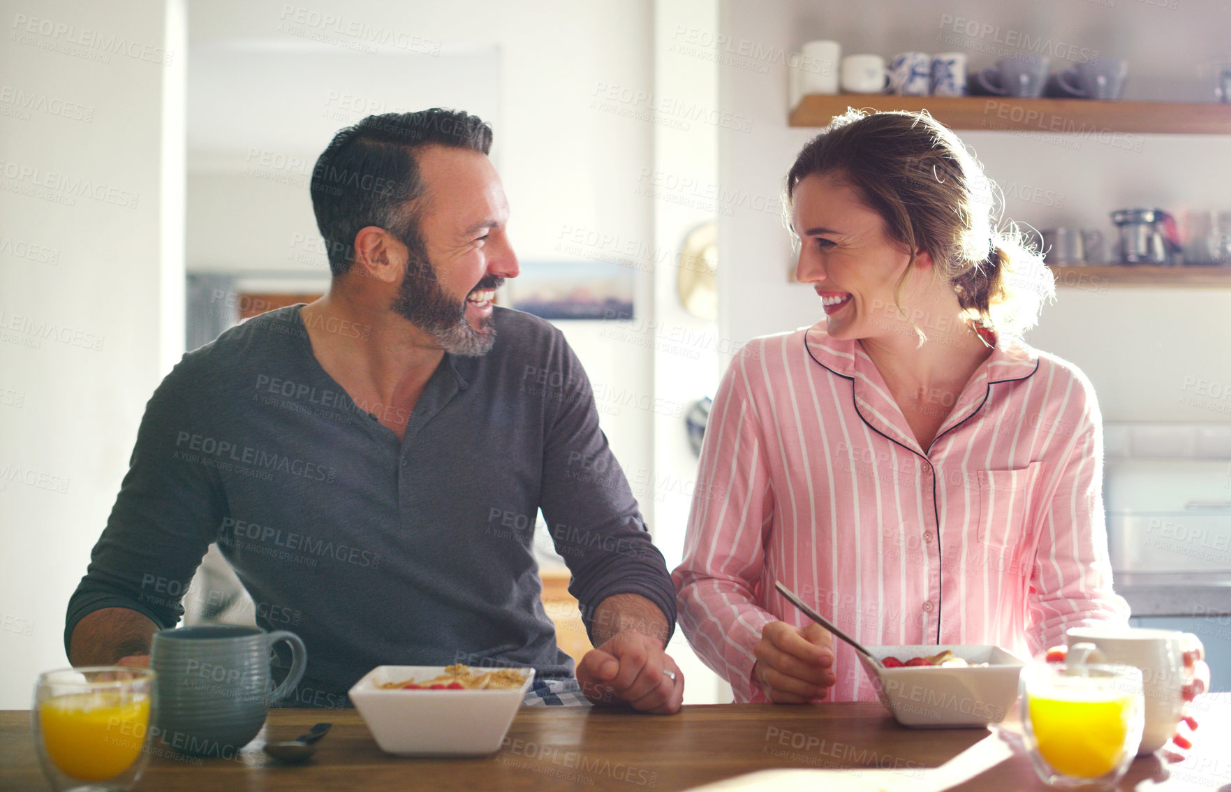 Buy stock photo Happy couple, laughing or eating breakfast with cereal, diet or juice in morning meal in home kitchen. People, trust or snack in bowl for bonding, funny joke and food in healthy marriage together