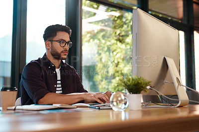 Buy stock photo Computer, serious and a business man typing and working at desk while online for research or creative work. Male entrepreneur person with glasses for reading or writing email with internet connection