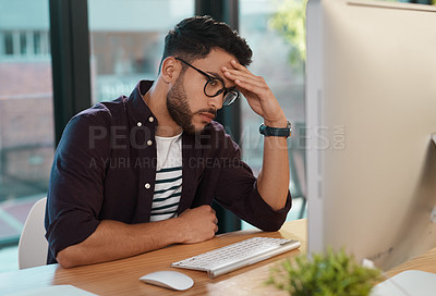 Buy stock photo Cropped shot of a handsome young businessman sitting alone in his office and feeling stressed while using his computer