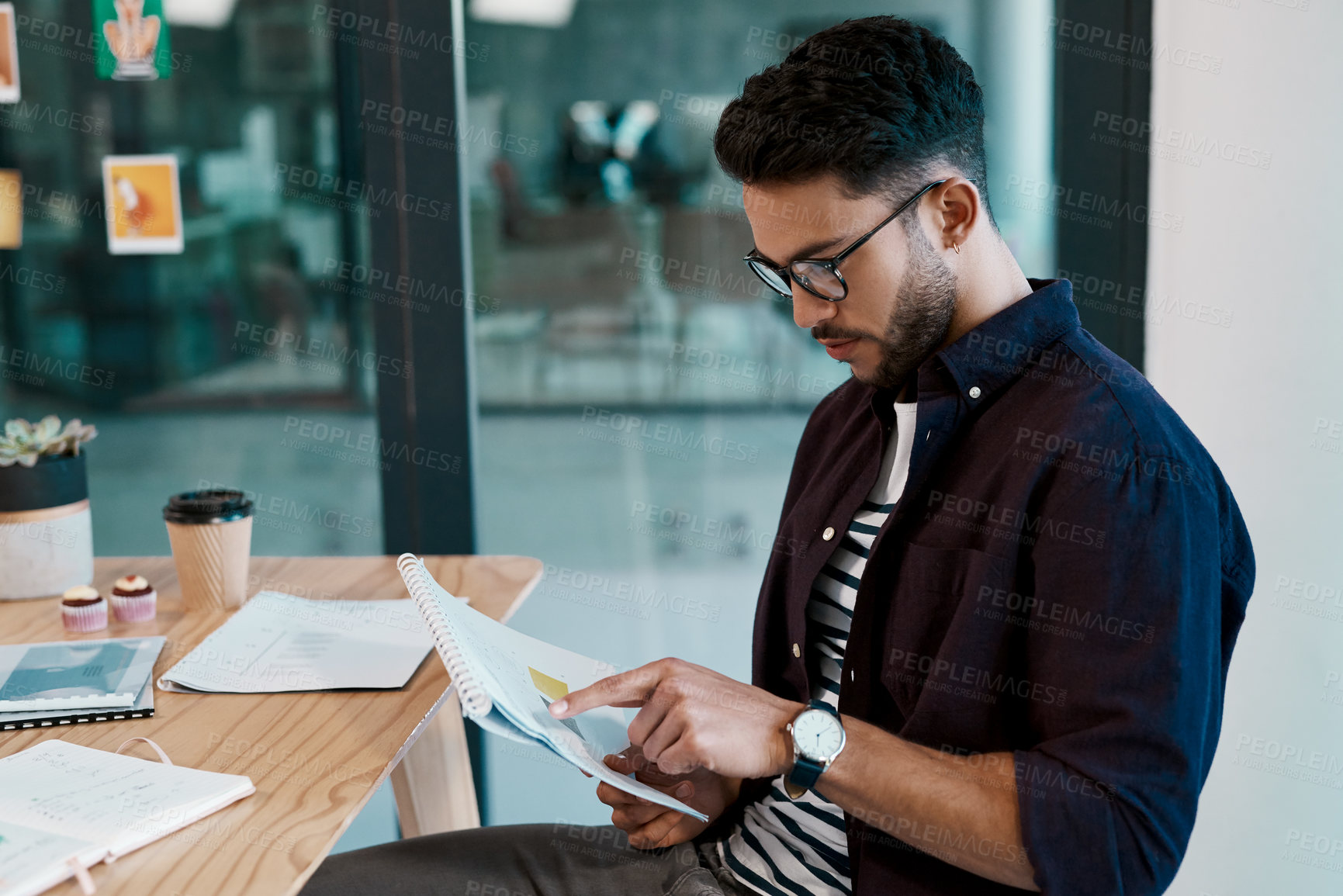 Buy stock photo Cropped shot of a handsome young businessman wearing spectacles and sitting alone in his office while reading paperwork