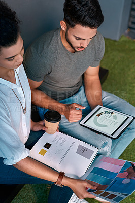 Buy stock photo Cropped shot of two young business colleagues sitting together and using a tablet while reading paperwork