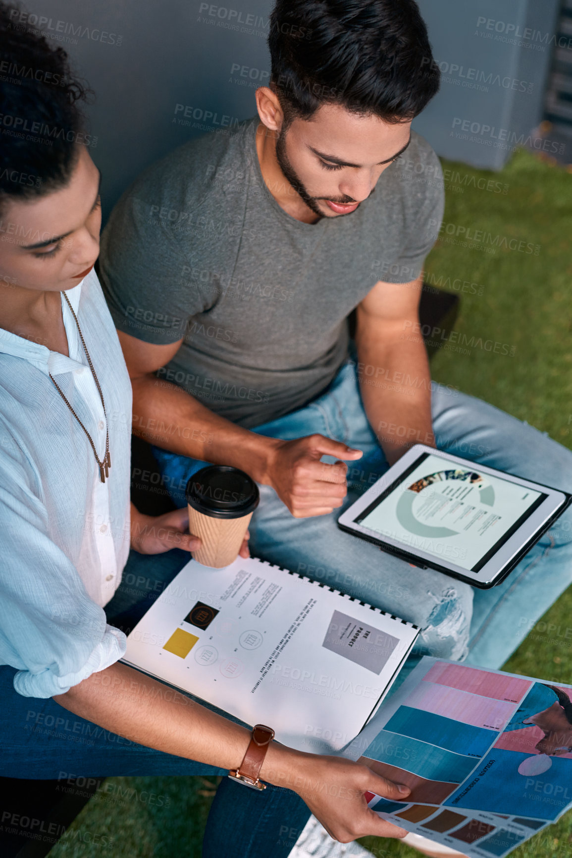 Buy stock photo Cropped shot of two young business colleagues sitting together and using a tablet while reading paperwork