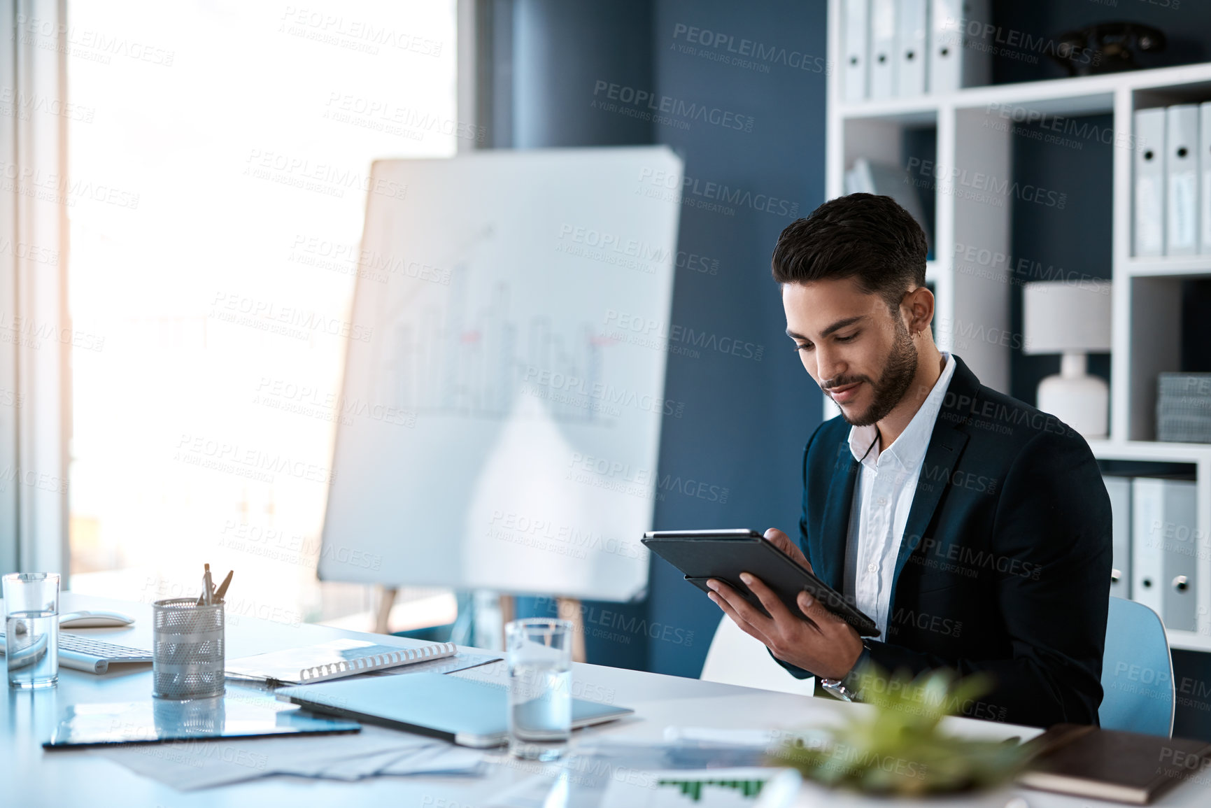 Buy stock photo Cropped shot of a handsome young businessman sitting alone and using a tablet in his office