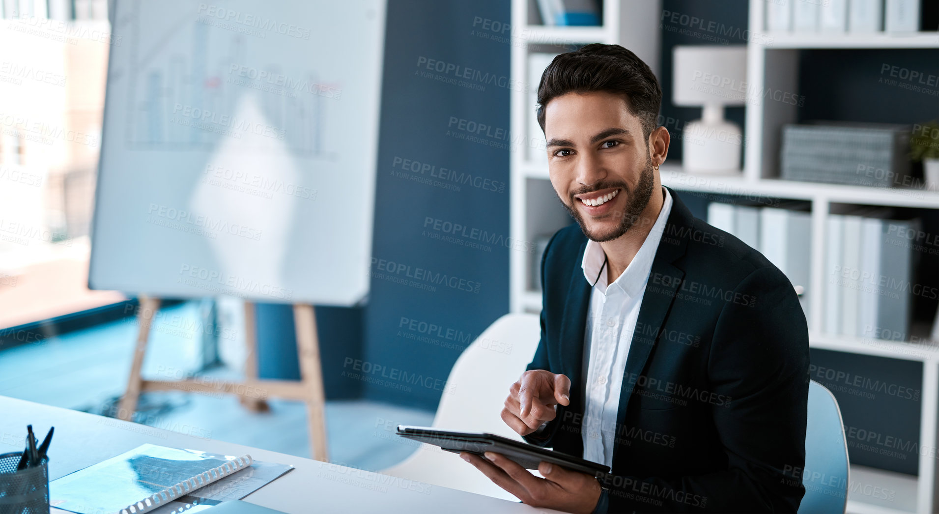 Buy stock photo Cropped portrait of a handsome young businessman sitting alone and using a tablet in his office